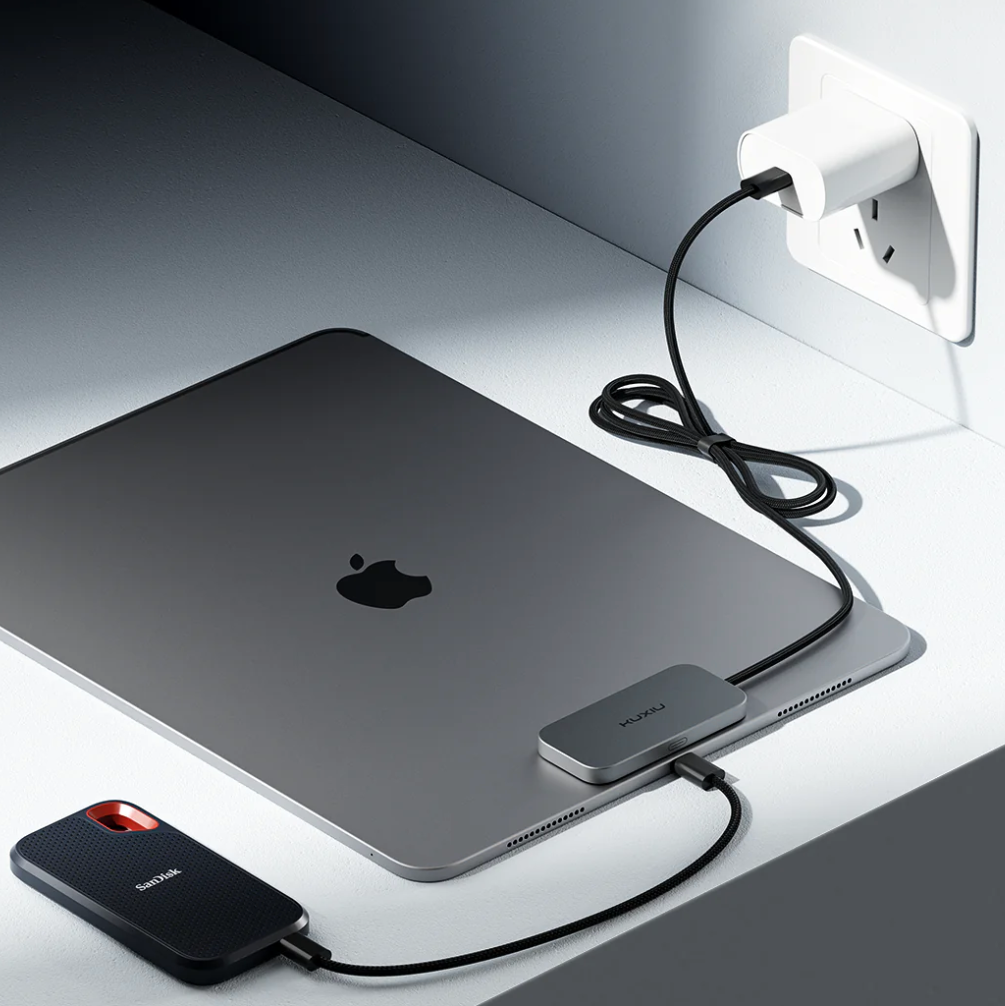 Apple laptop with magnetic attachment with cables leading to the wall and to a phone.